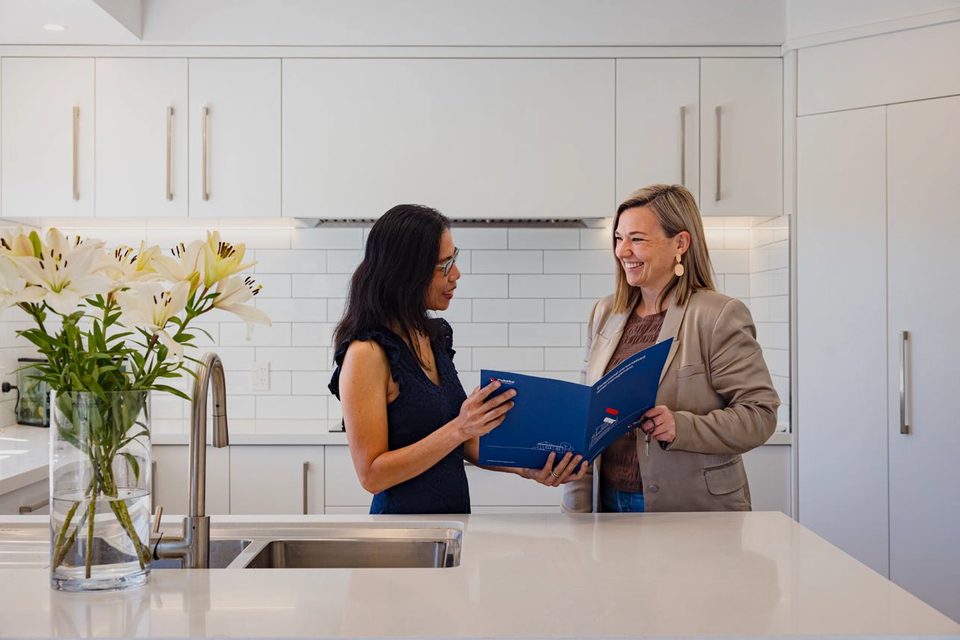 A property owner and a rental manager reviewing paperwork in a management folder at a kitchen bench.