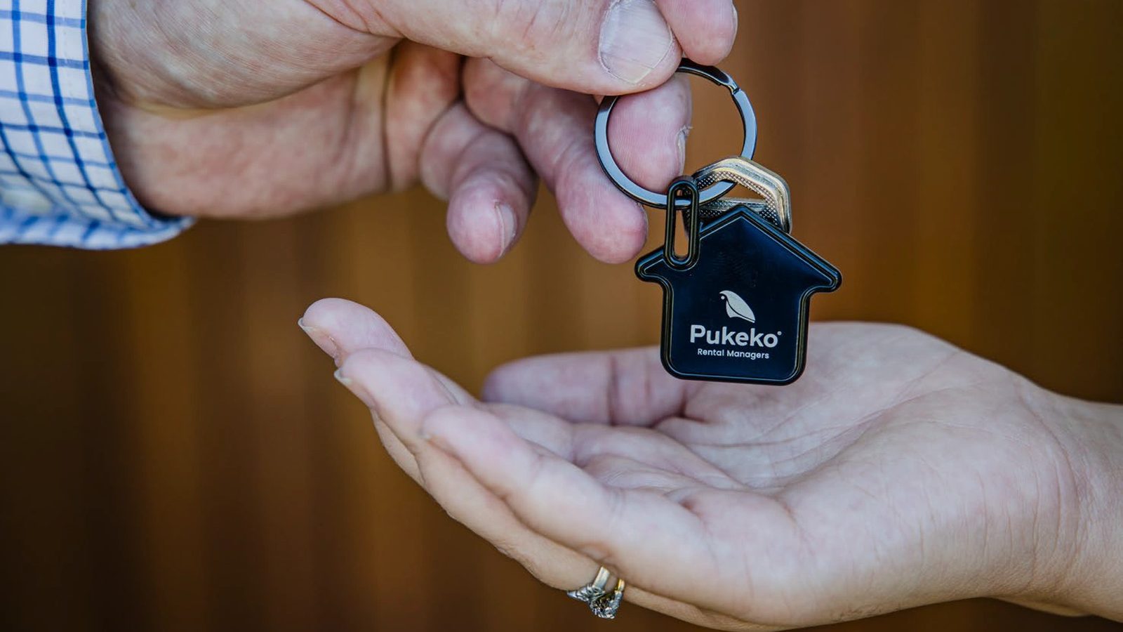 A Pukeko Rental Managers house-shaped keyring being handed from one person to another's open palm.