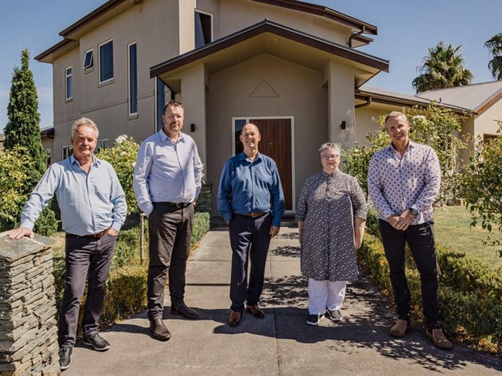 Five Pukeko rental managers standing on the front path of a two-storey rendered home.
