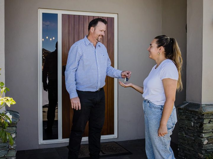 A rental manager handing a set of keys to a new tenant at the front door of a house.